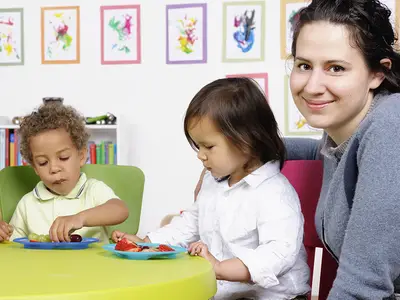 Three preschoolers eat fruit at a table with a teacher.