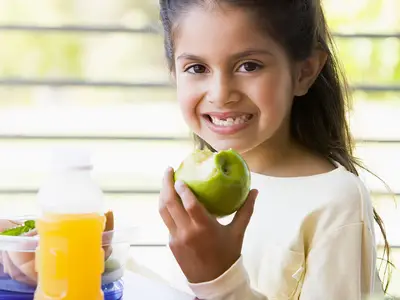A kindergarten-age girl smiles while eating her lunch.