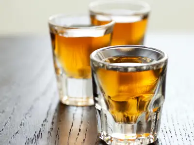 Glasses of whiskey sit on a wooden bar counter.