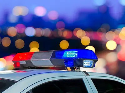 Red and blue lights from a police car flash against the background of a city skyline.