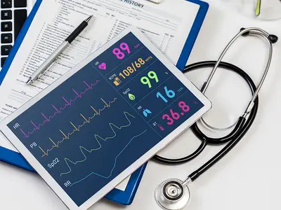 A display representing the transition to electronic health records, including a tablet showing a patient's vital signs and a clipboard of their medical history.