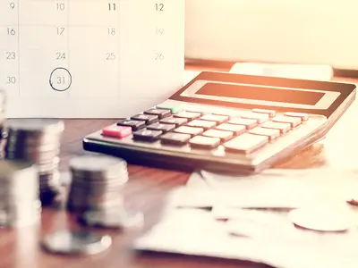 Photo illustration of a calendar, calculator, and money on a desk.
