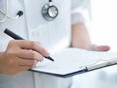 A closeup of a doctor in a lab coat checking items off of a list on a clipboard.