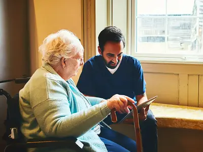 A senior woman and a male caregiver look at photos on a tablet.