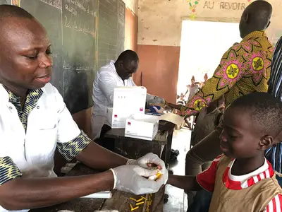 A young boy has his finger pricked during a transmission assessment survey for lymphatic filariasis at a school in Benin. Photo by Katie Zoerhoff for RTI International 