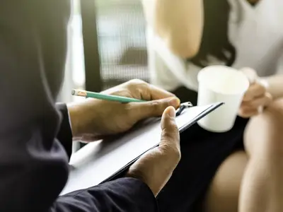 Closeup of a researcher taking notes on a clipboard while interviewing someone.