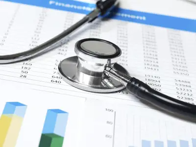 Stethoscope resting on financial documents with charts and graphs in a medical setting.
