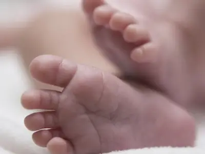 Tiny baby feet curl softly on a white blanket in a tranquil setting.