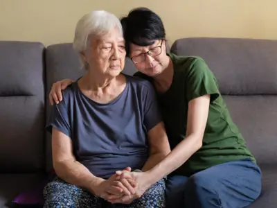 Daughter consoles elderly mother on couch