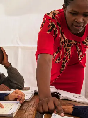 Teacher helping student with workbook. Two other students sitting beside