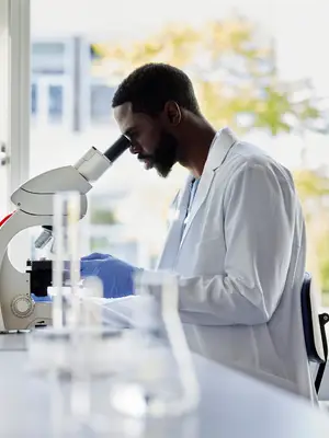 Photo of a Black scientist in a lab looking into a microscope