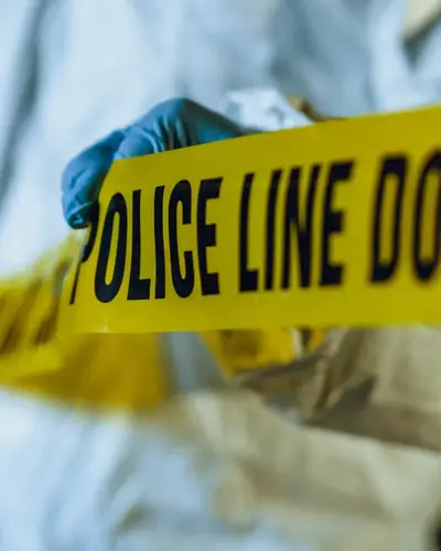 Photo of a forensic investigator unrolling police tape to mark off a crime scene