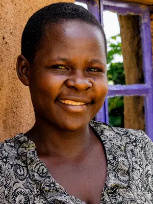 A smiling Kenyan woman standing outside a house.