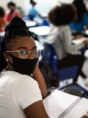 Photo of a classroom with a masked student taking notes in the foreground.