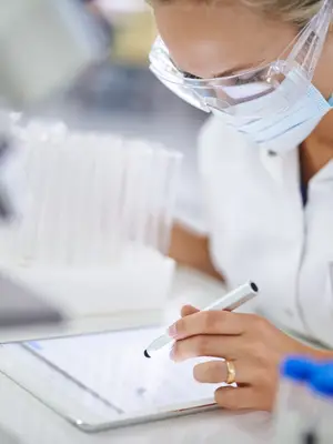 Photo of a woman scientist in a laboratory using a tablet to take notes