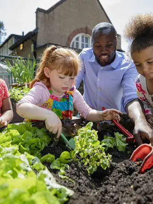 Photo of preschool students and a teacher working in a garden.