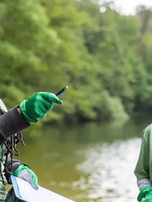 Women with wearing rubber gloves with community members cleaning up the shore of a lake