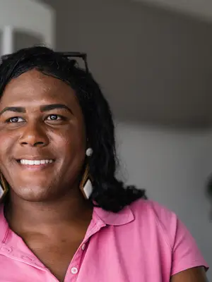 Photo of a trans woman wearing a pink blouse and dangly earrings with glasses on her head.