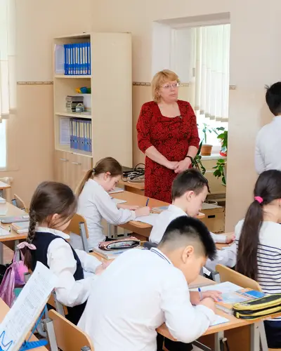 Students write at their desks while a teacher demonstrates concepts on a whiteboard.