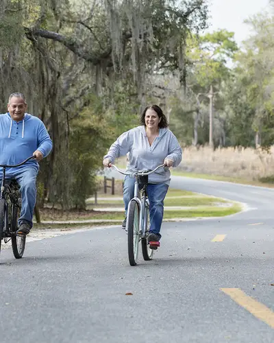 A middle-aged couple riding bikes along a tree-lined road in rural Florida.