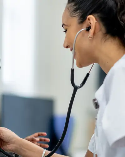 A child smiles while a doctor checks his heartbeat with a stethoscope.