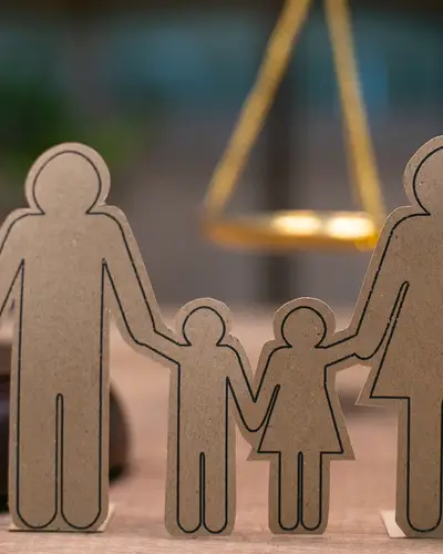 Paper cutouts representing a family stand in front of a judge's gavel and a set of scales.