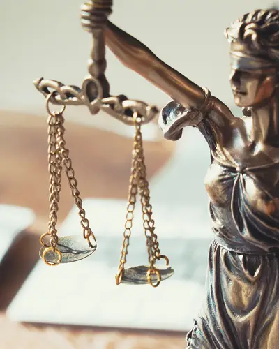 A small bronze sculpture of blindfolded Lady Justice stands on a desk with a computer and mouse.