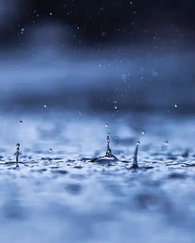 Rain drops falling into puddle on the ground