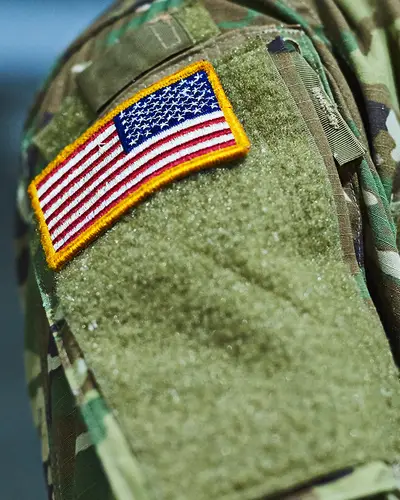 A closeup of a U.S. soldier in camouflage clothing with an American flag patch on the shoulder.