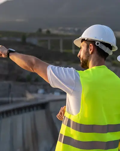 Three engineers in safety gear look out over the top of a large dam.