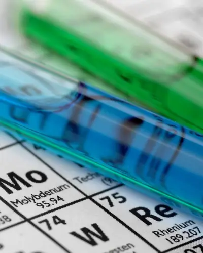 A closeup of two test tubes containing brightly colored liquids and sitting on a copy of the Periodic Table.