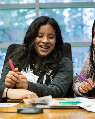 Three girls laugh as they work on a project together