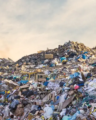 A bulldozer sits atop a heap of garbage in a large landfill.