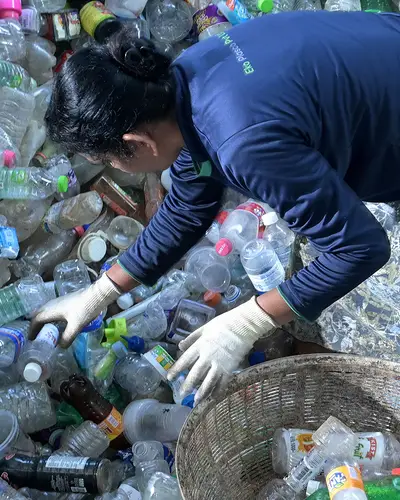 A woman collects bottles from a heap of plastic waste.
