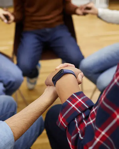 A closeup of a circle of people holding hands, as if participating in a support group.