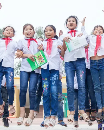 Schoolchildren in Vietnam hold hands, smile, and jump.