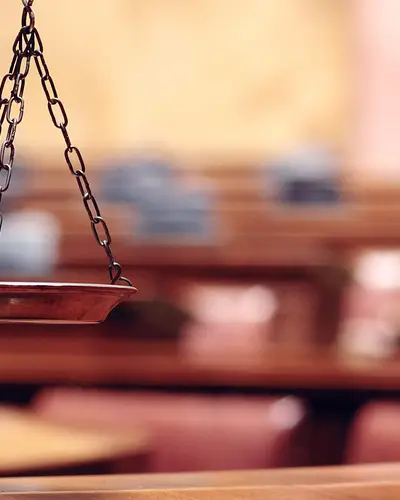 Bronze scales of justice before a courtroom background.