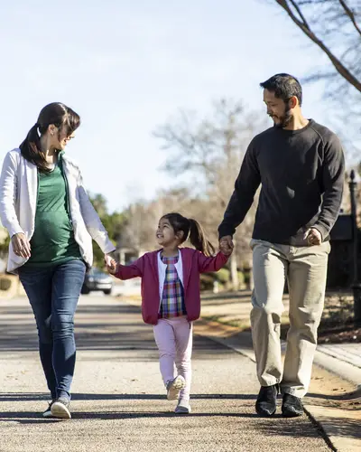 Photo of mother, father, and child holding hands on a walk
