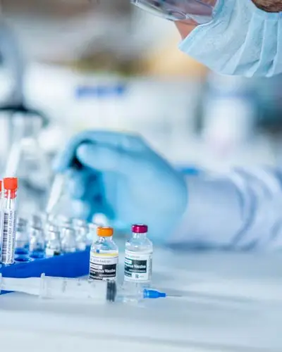 Photo of a scientist in PPE with a pipette and a rack of test tubes and vials