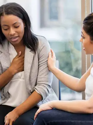 Photo of a woman speaking and holding her chest while being comforted by a counselor