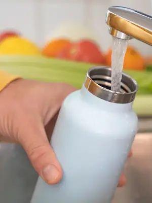 Hand holding water bottle under water faucet