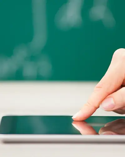 A person uses a tablet in front of a chalkboard in a classroom