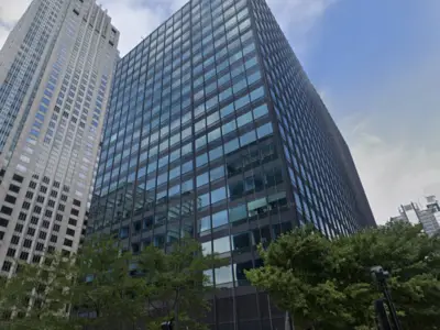 A tall, glass-covered building reflects surrounding skyscrapers under a clear blue sky.