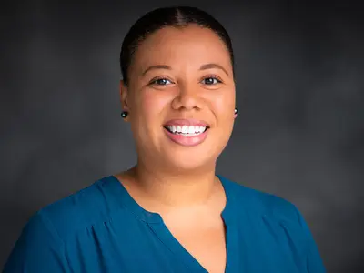 Headshot of Imari Walker-Franklin smiling against a dark background