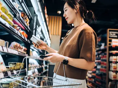 A woman inspects a label while shopping at a grocery store.