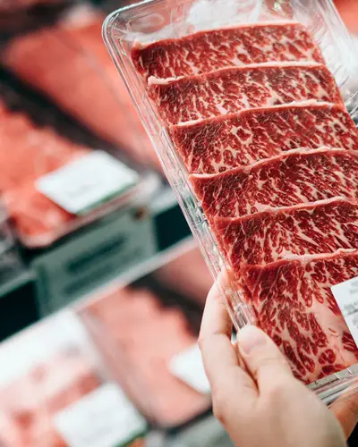 Hand holding a package of red meat in the meat section at a grocery story