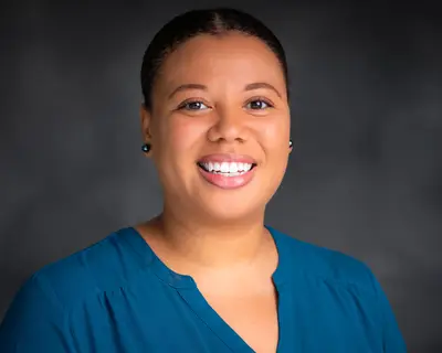 Headshot of Imari Walker-Franklin smiling against a dark background