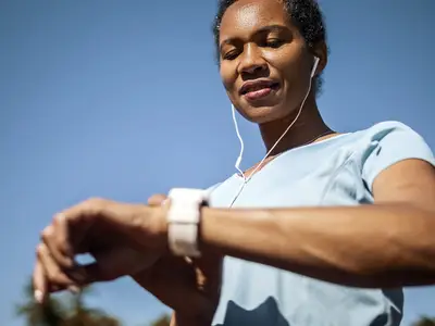 Photo of jogger looking at smartwatch and wearing earbuds.