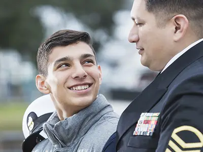 A teenage boy looks proudly at his father in his Navy uniform.