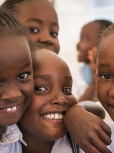 Children smile and hug while participating in the Tusome reading program.